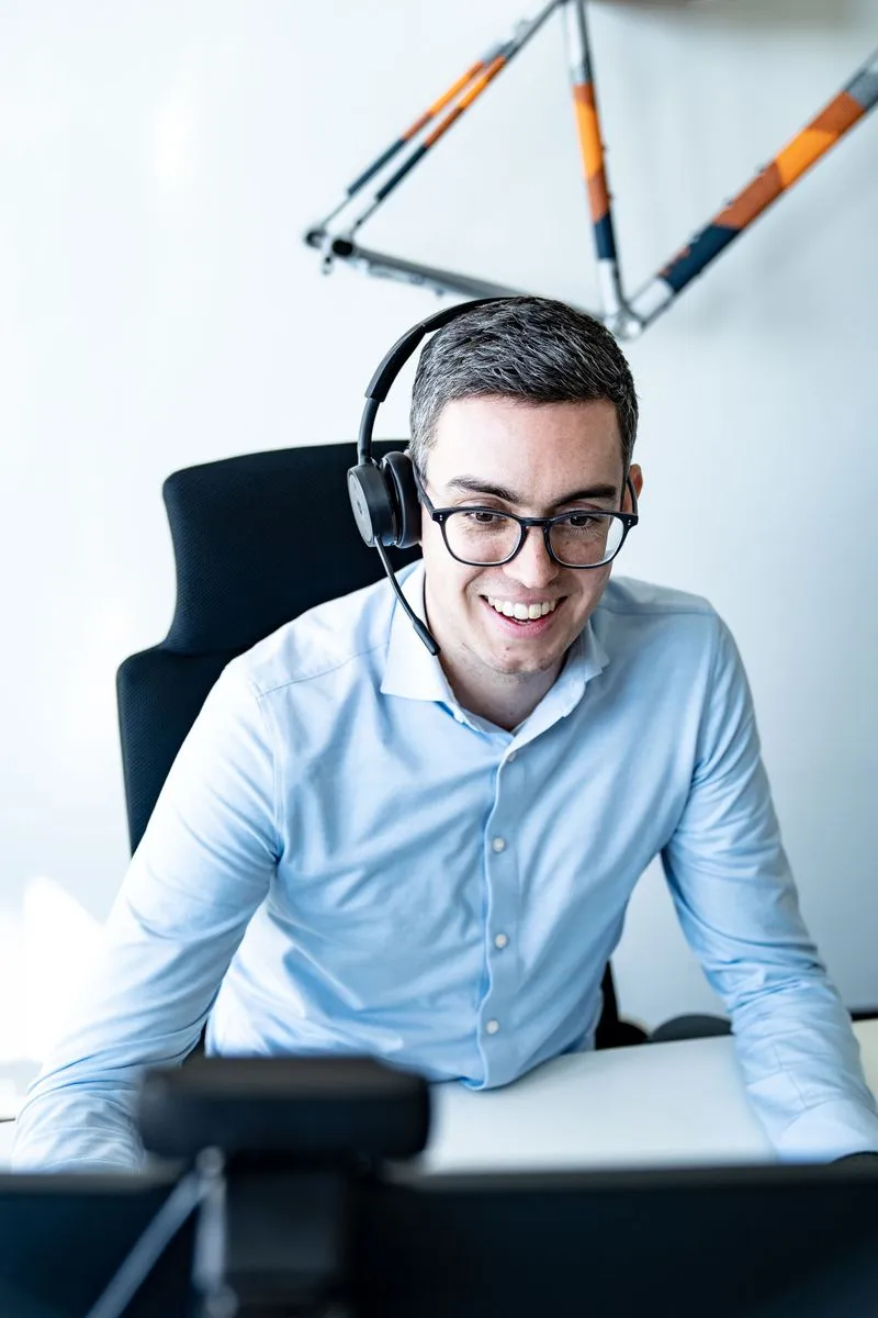 Mann mit Headset und Brille im Büro, Online-Meeting am Computer, lächelnd